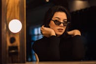 一位戴着太阳镜的优雅女士，在昏暗的室内时尚地摆着姿势，展现其别致的时尚与态度