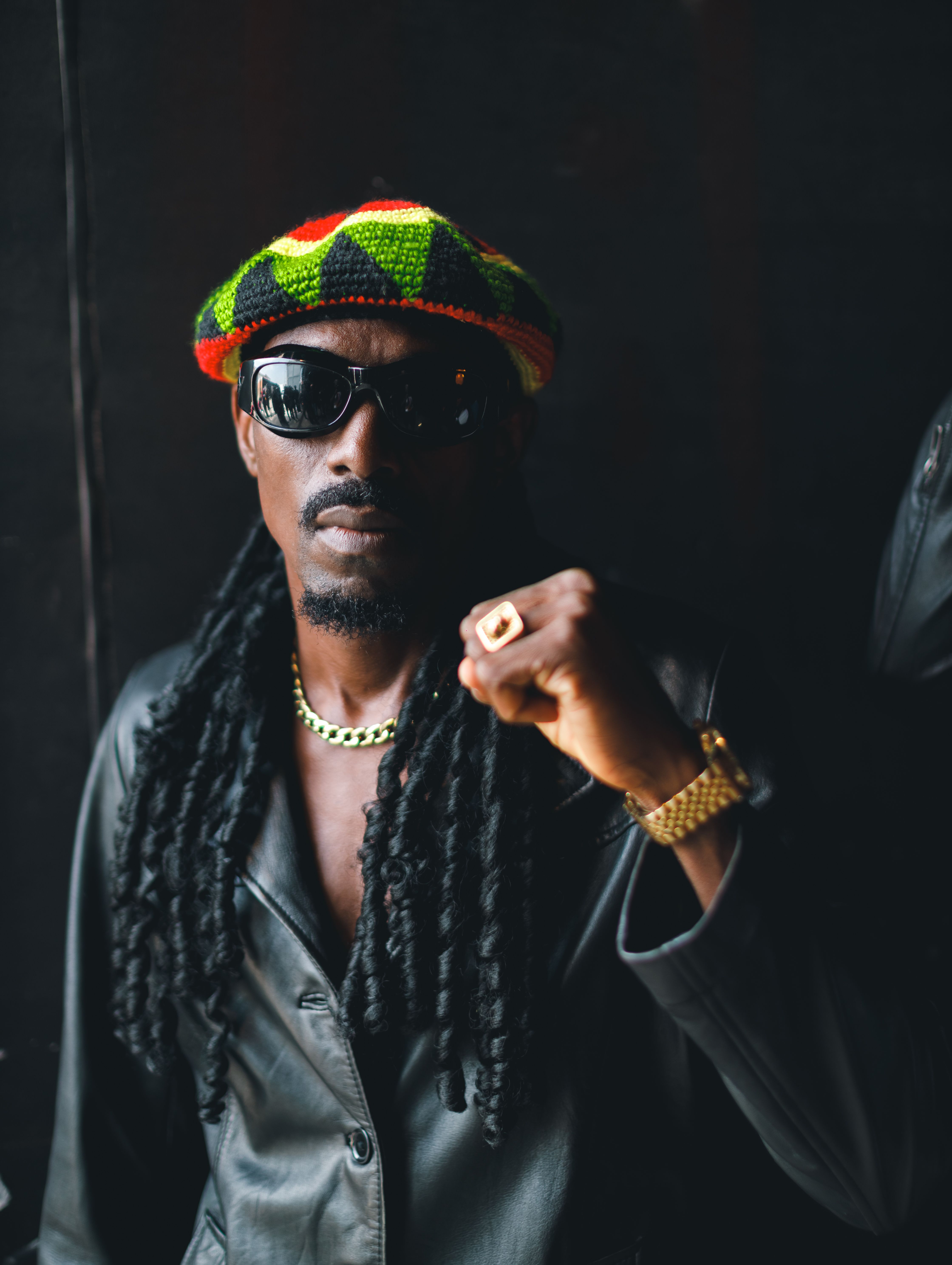 Close-up portrait of an African man wearing sunglasses, a leather jacket, and a colorful knit hat.
