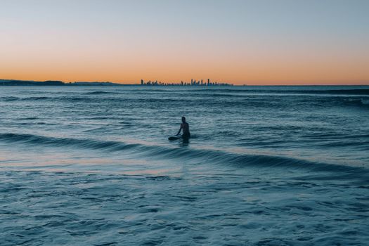 A lone surfer enjoying the tranquil waves at sunset in Coolangatta, QLD, Australia.