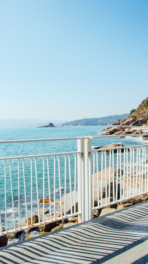 Free Bright seaside view from a white railing with rocks and clear sky. Stock Photo