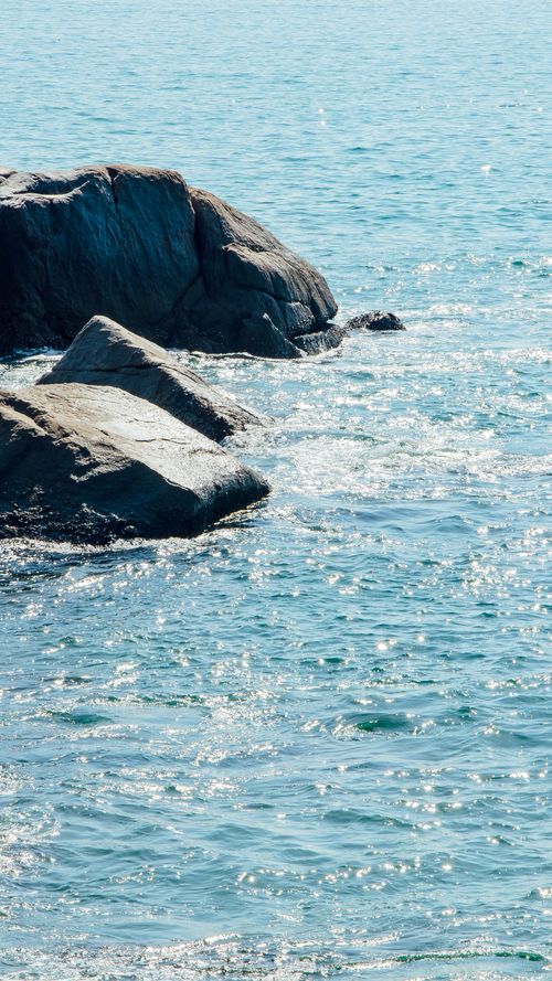 Free Peaceful ocean scene with rocky shoreline and sparkling blue water under bright sunlight. Stock Photo