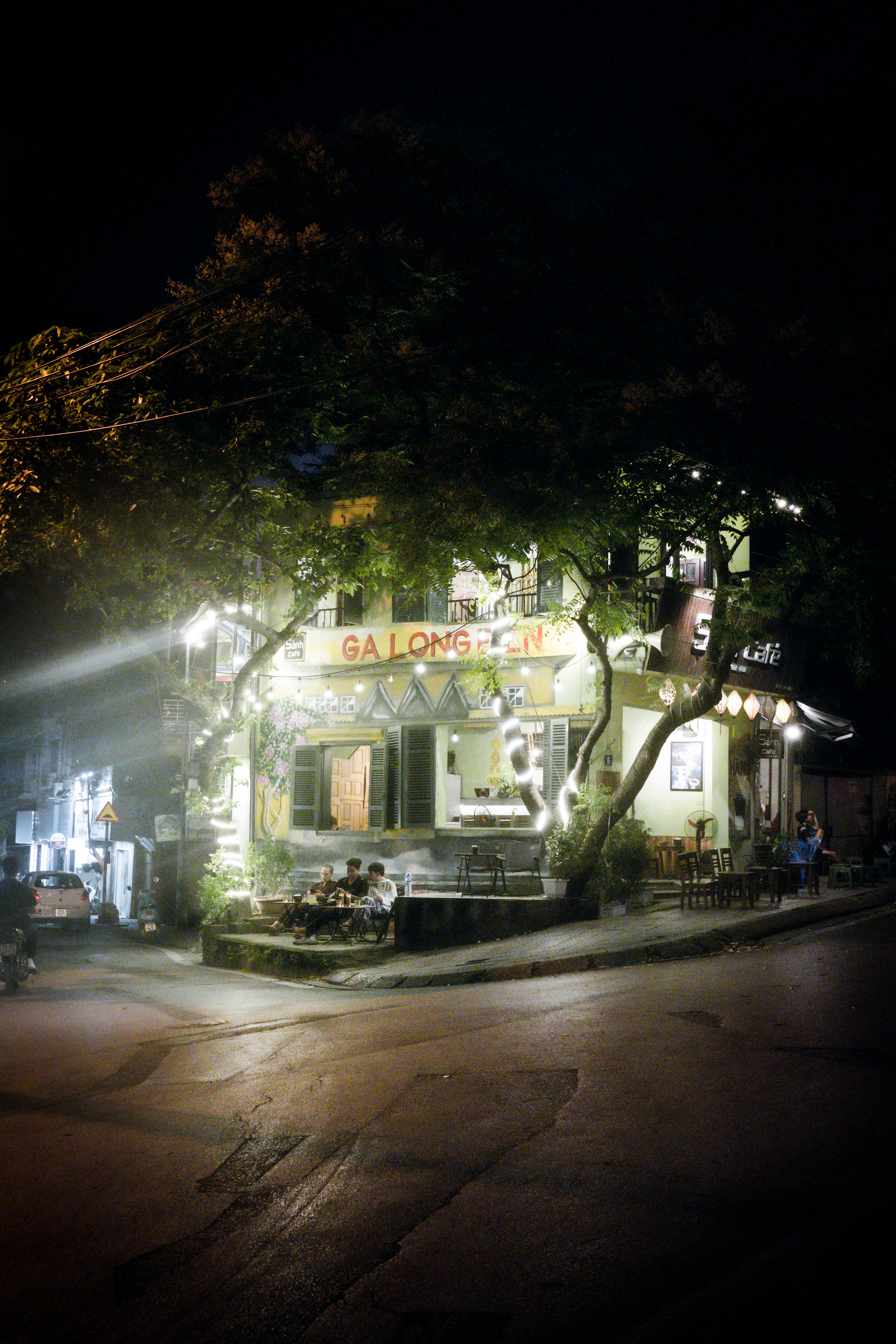 Free A cozy urban street corner at night featuring illuminated cafés and people enjoying evening ambiance. Stock Photo