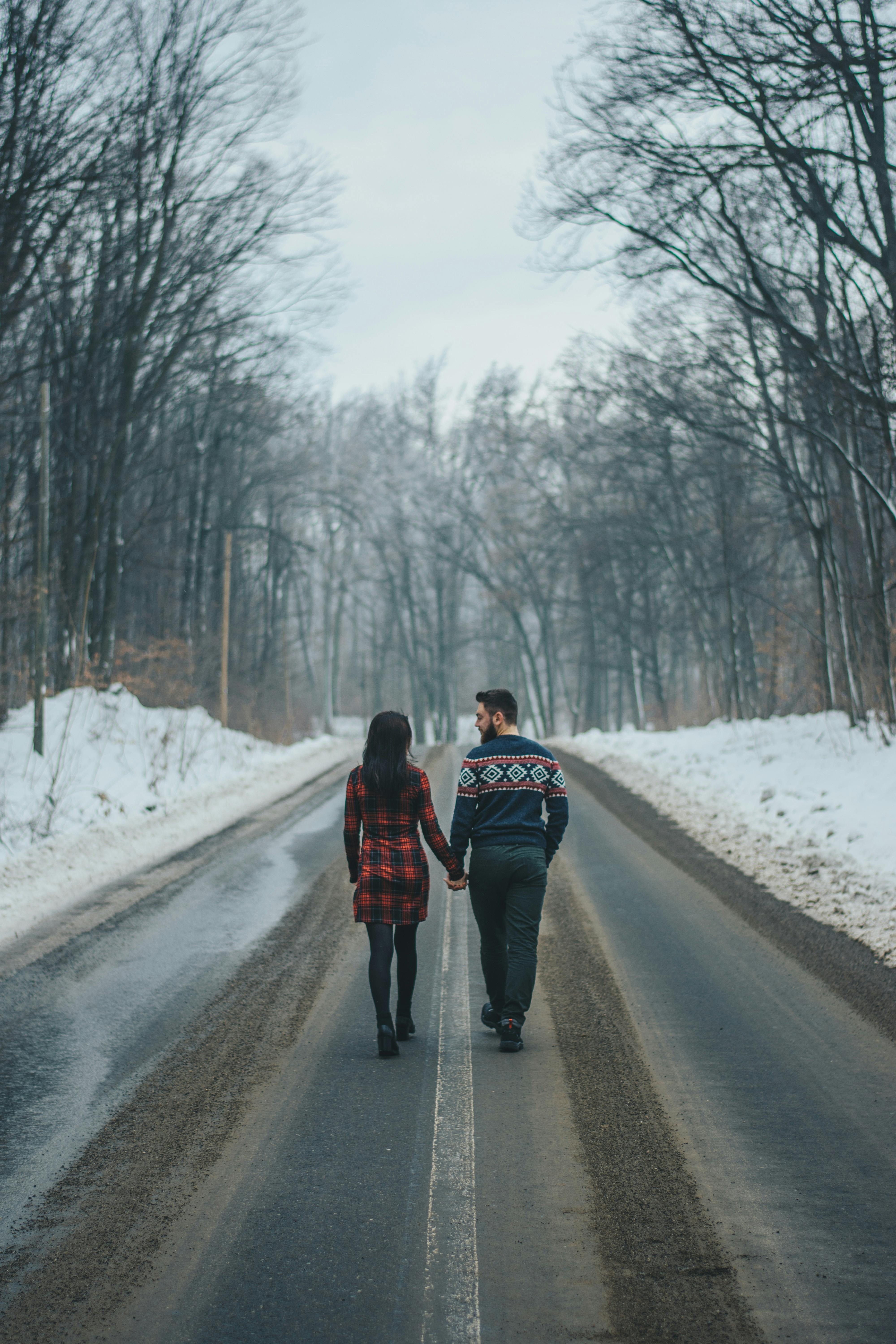 photo of couple walking on road near bare trees