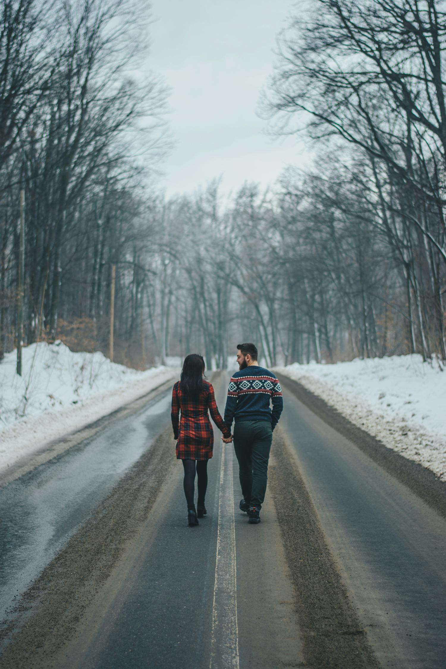 裸の木の近くの道路を歩いているカップルの写真