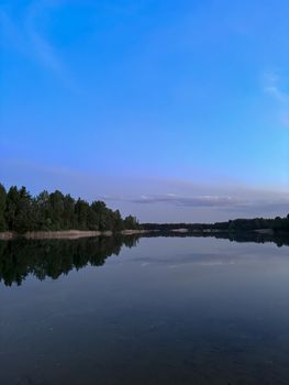 Calm lake reflecting the clear blue sky and lush trees at dusk.
