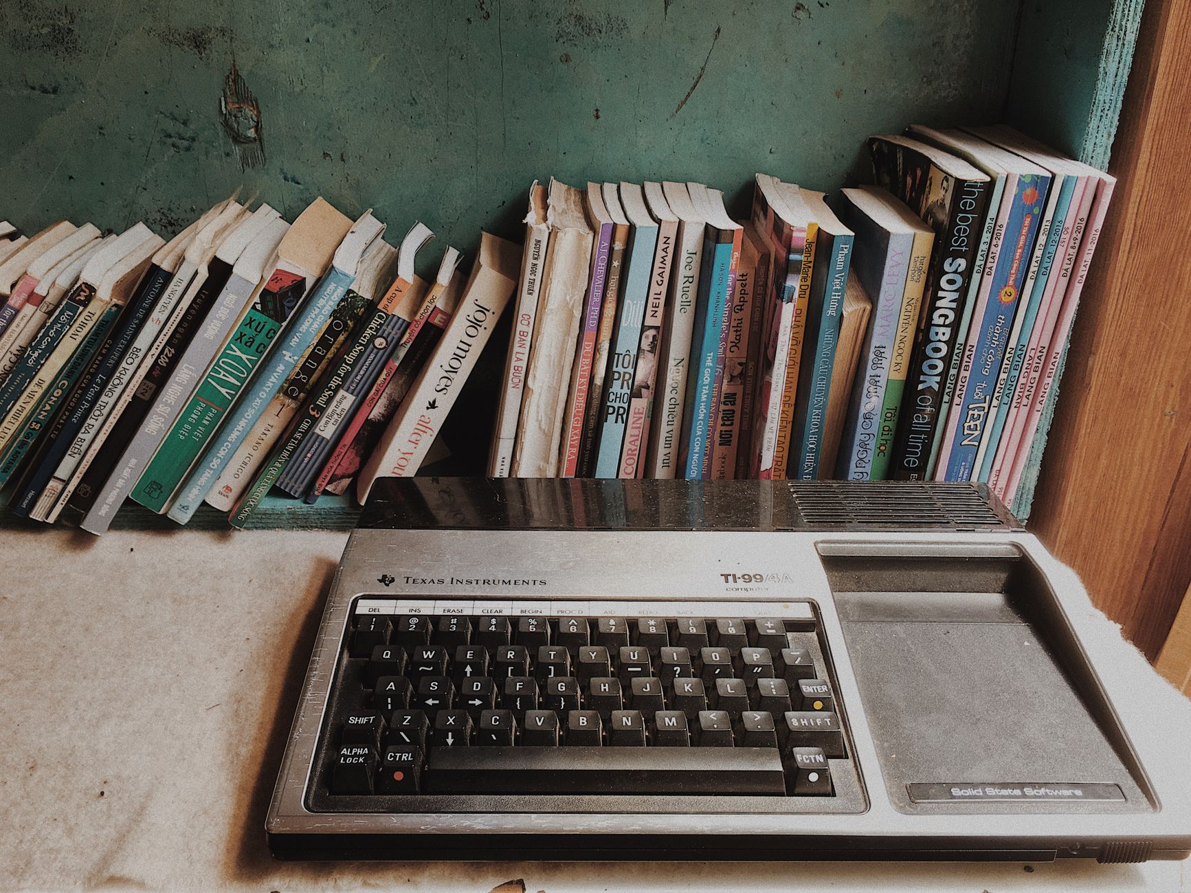 A retro Texas Instruments computer surrounded by a variety of books, showcasing a blend of technology and literature in a home setting.