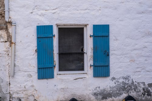 A white wall with blue shutters and a blue door