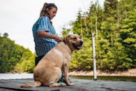 一个女人带着她的狗，在平静湖边的码头上，四周环绕着郁郁葱葱的绿色植物