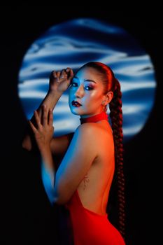 Elegant woman in a red dress with a long braid against a blue light backdrop.