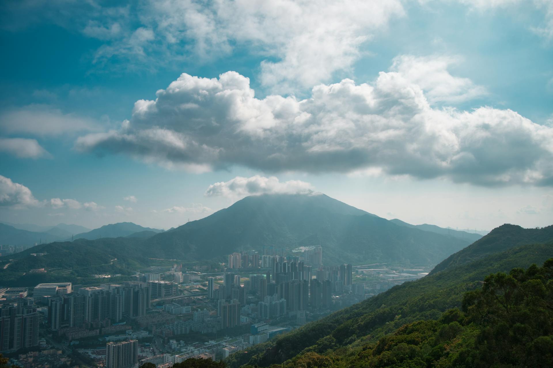 Breathtaking view of Shenzhen city skyline surrounded by lush green mountains and dramatic clouds.