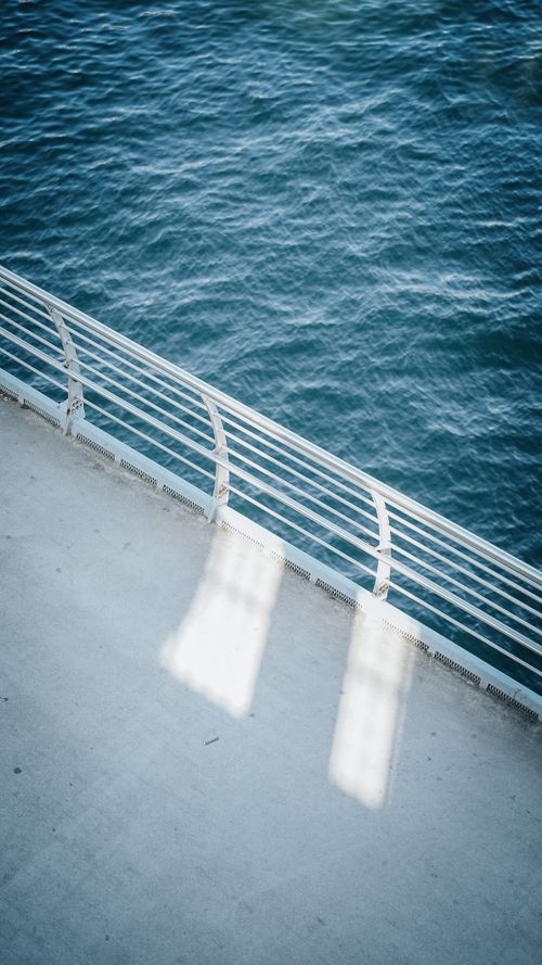 Free A calming view of blue ocean water seen through ferry deck railings, with shadows cast on the walkway. Stock Photo