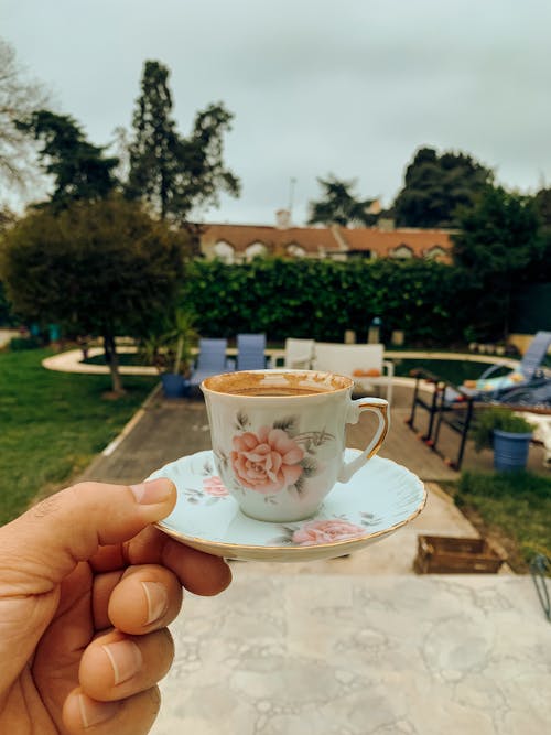 A person holding a cup of coffee in front of a garden