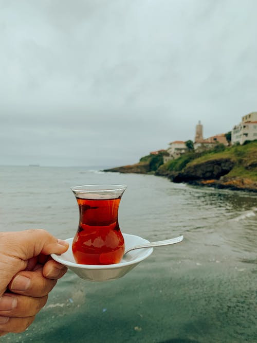 A person holding a cup of tea over the ocean