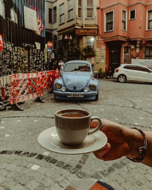 A person holding a cup of coffee in front of a car