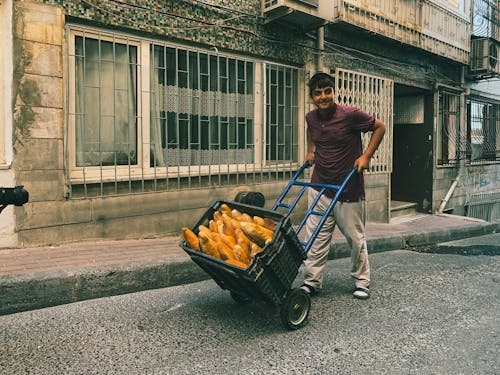 A man pushing a cart with a bag of corn on the street