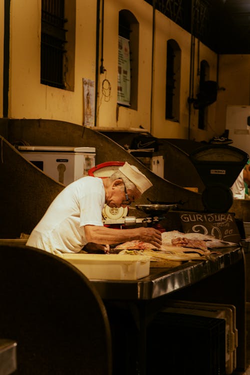 A man in a white hat is cutting food