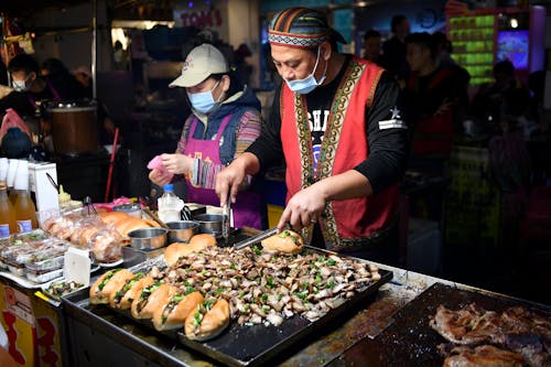 Two people in face masks are preparing food at an outdoor market