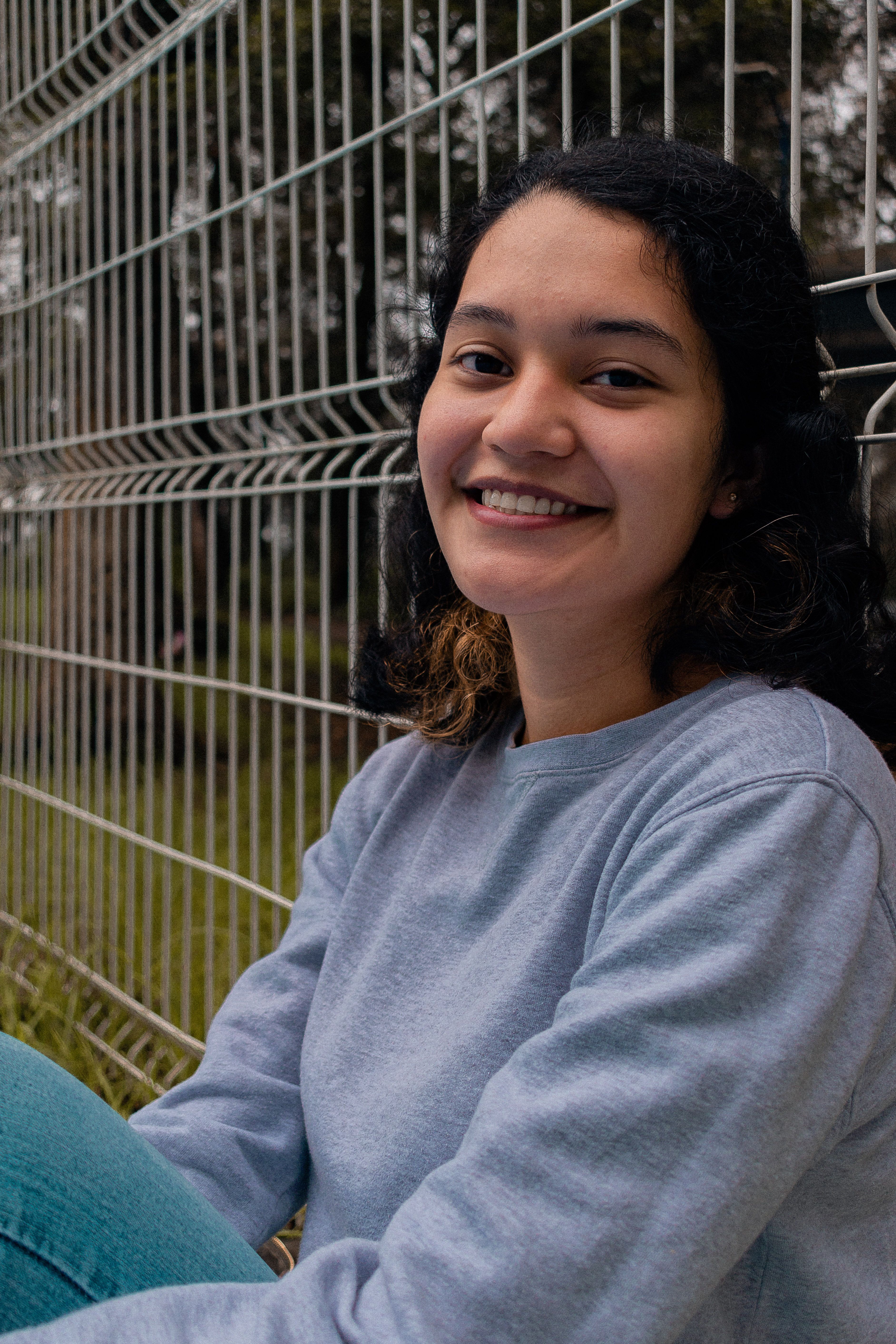 A cheerful young woman in a grey sweater smiling outdoors in Teziutlán, Mexico.