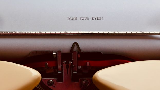 Close-up of a vintage typewriter with paper displaying 'Damn your eyes!' text.