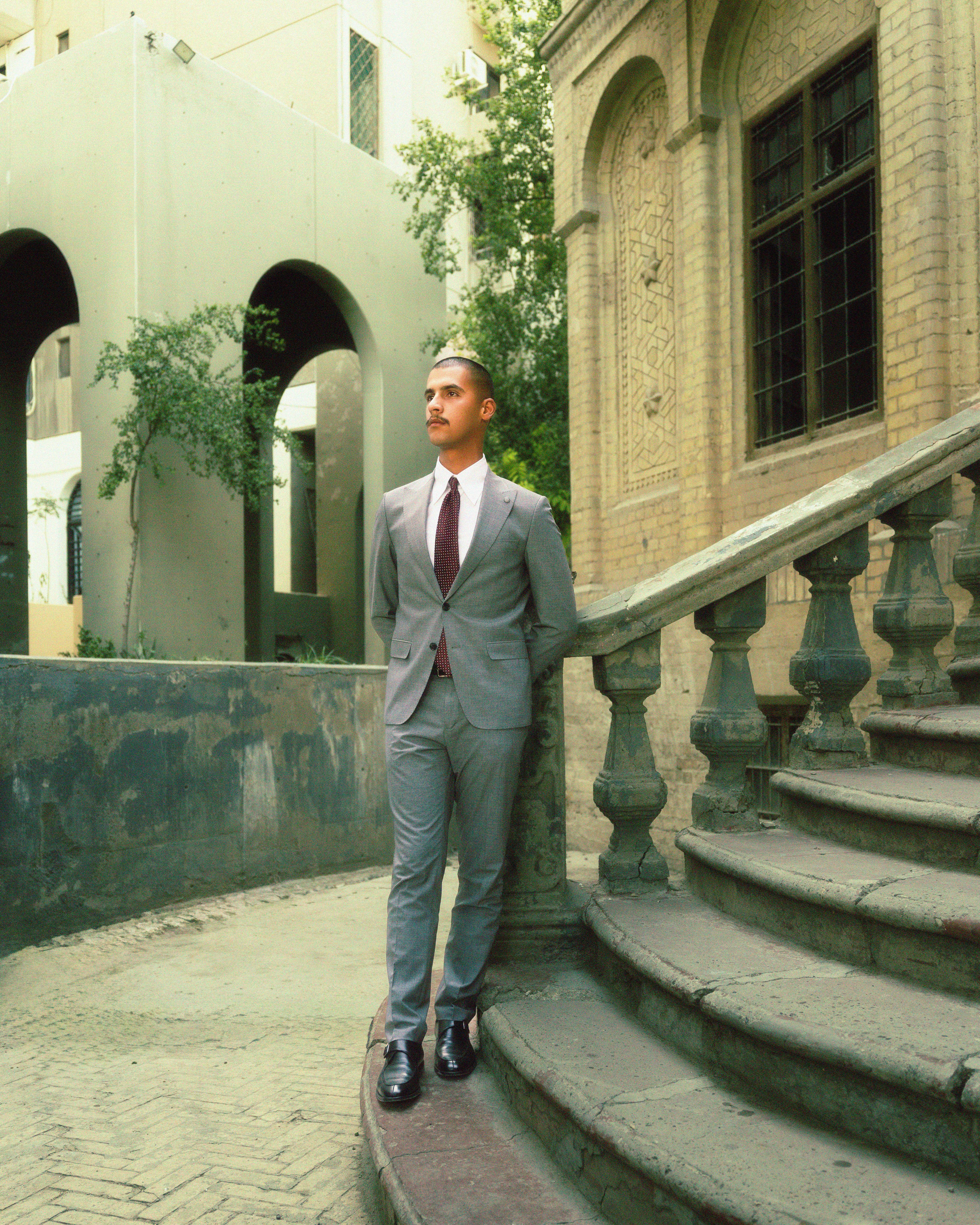 Elegantly dressed man in a modern grey suit standing on outdoor urban stairway.