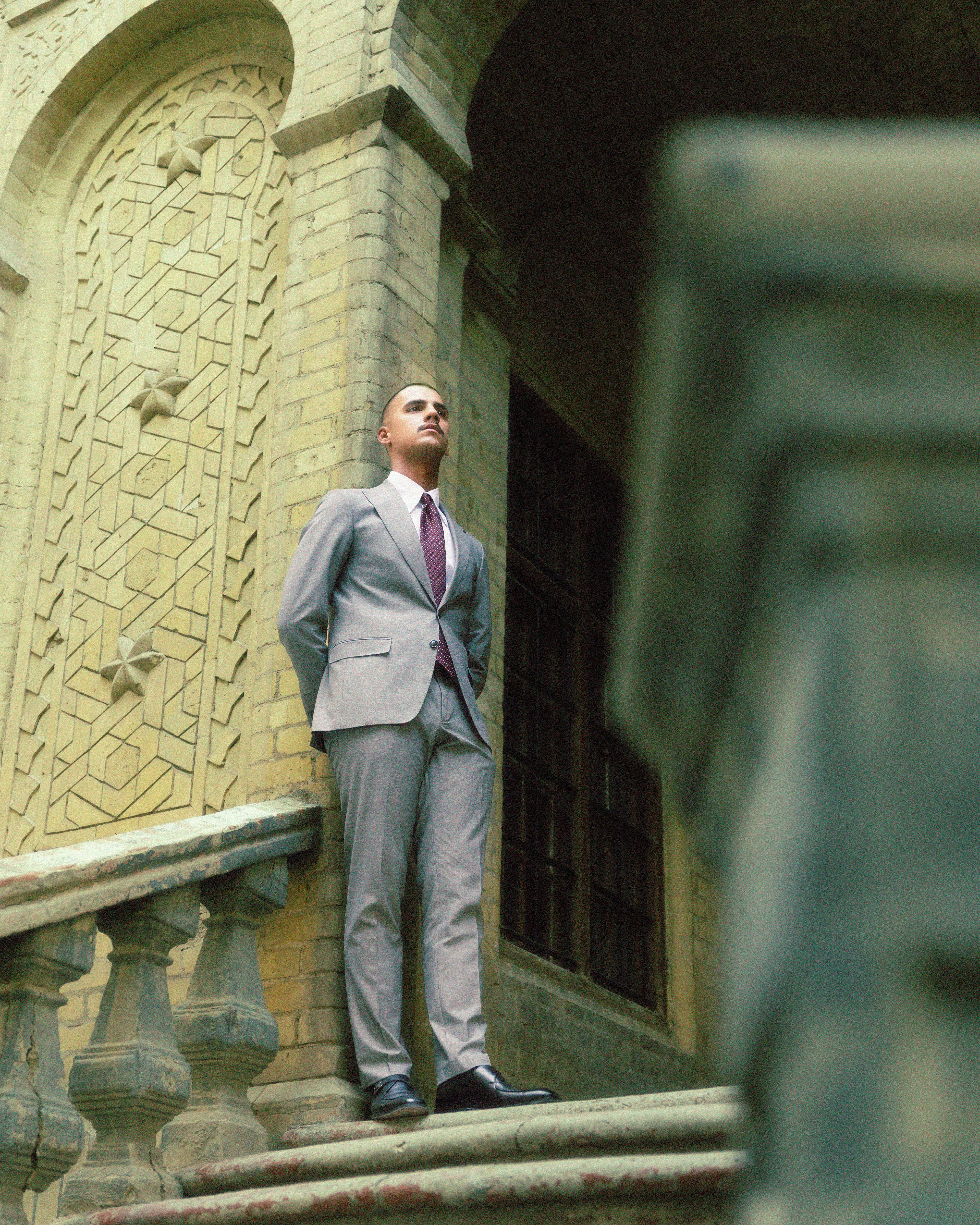A stylish man in a suit posing on a historic building's staircase, exuding confidence and elegance.