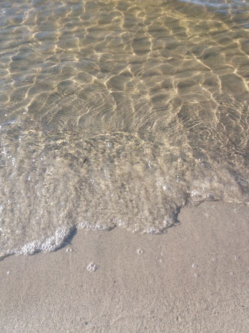 Free Gentle waves softly lap against a sandy, sunlit beach shoreline, creating a tranquil coastal scene. Stock Photo