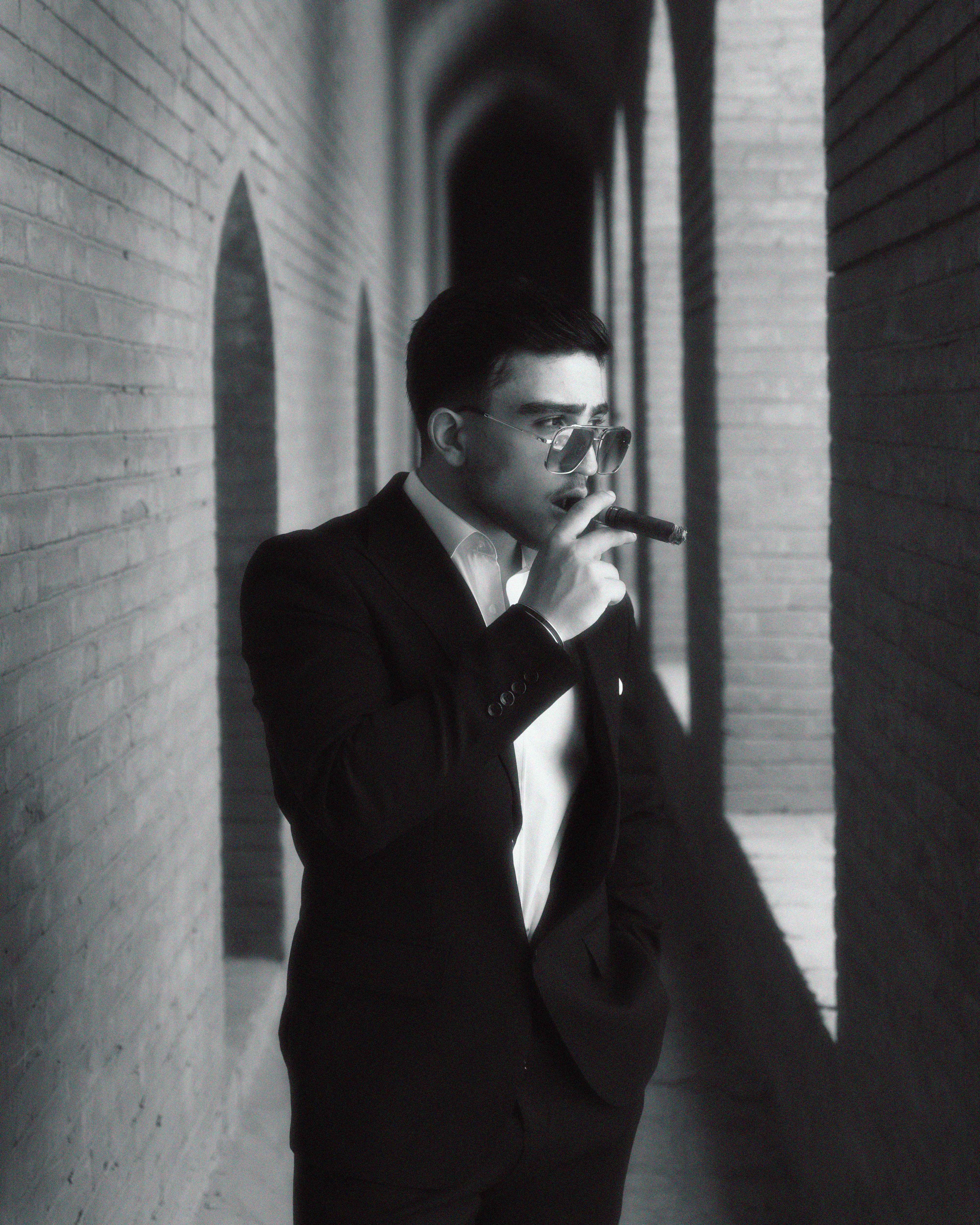Man in tuxedo with sunglasses in a brick corridor, exuding confidence.