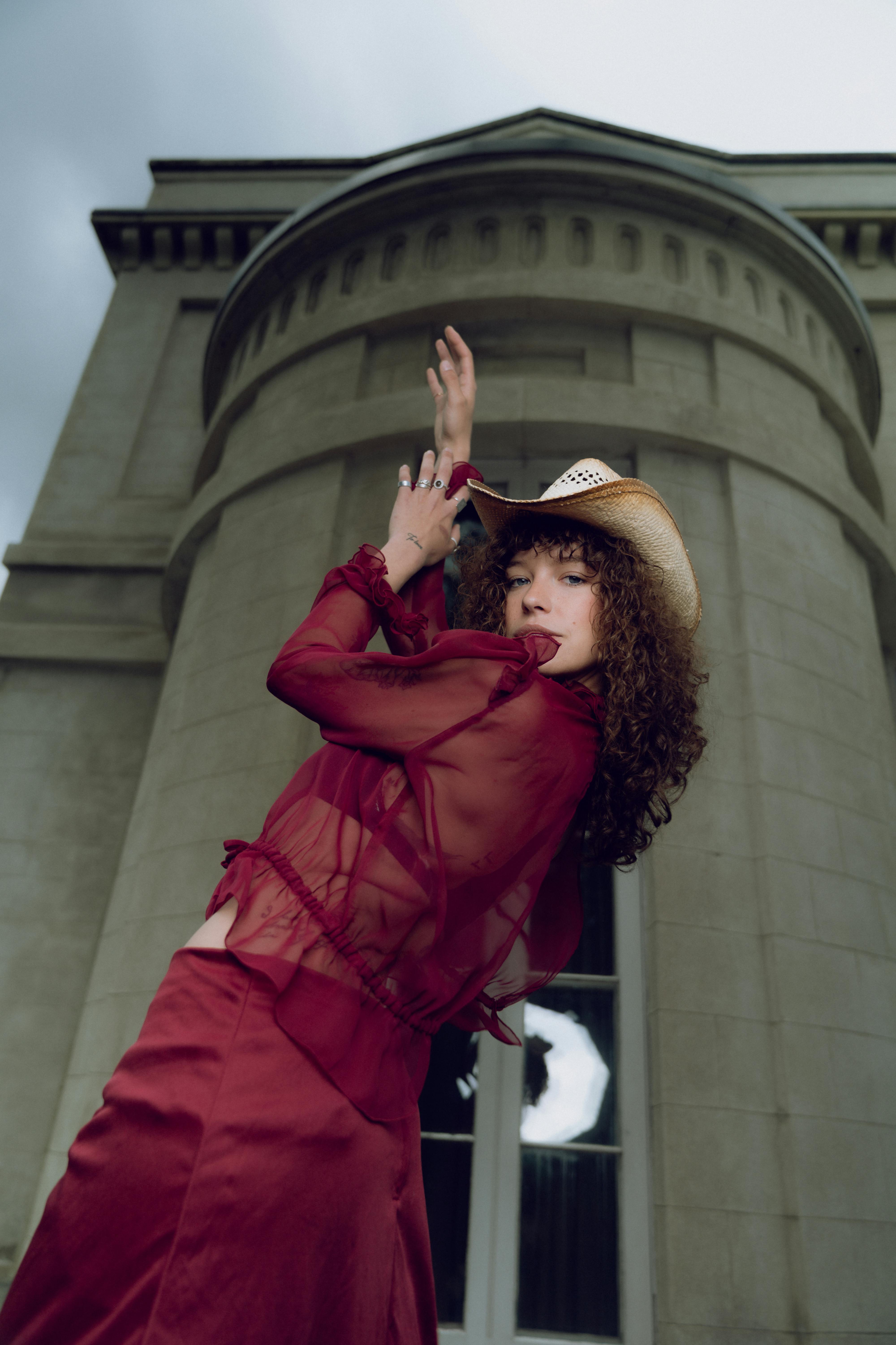 a woman in a red dress and hat is throwing her arms up