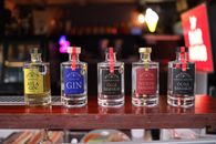 A close-up look at five artisanal gin bottles displayed on a wooden bar counter indoors.