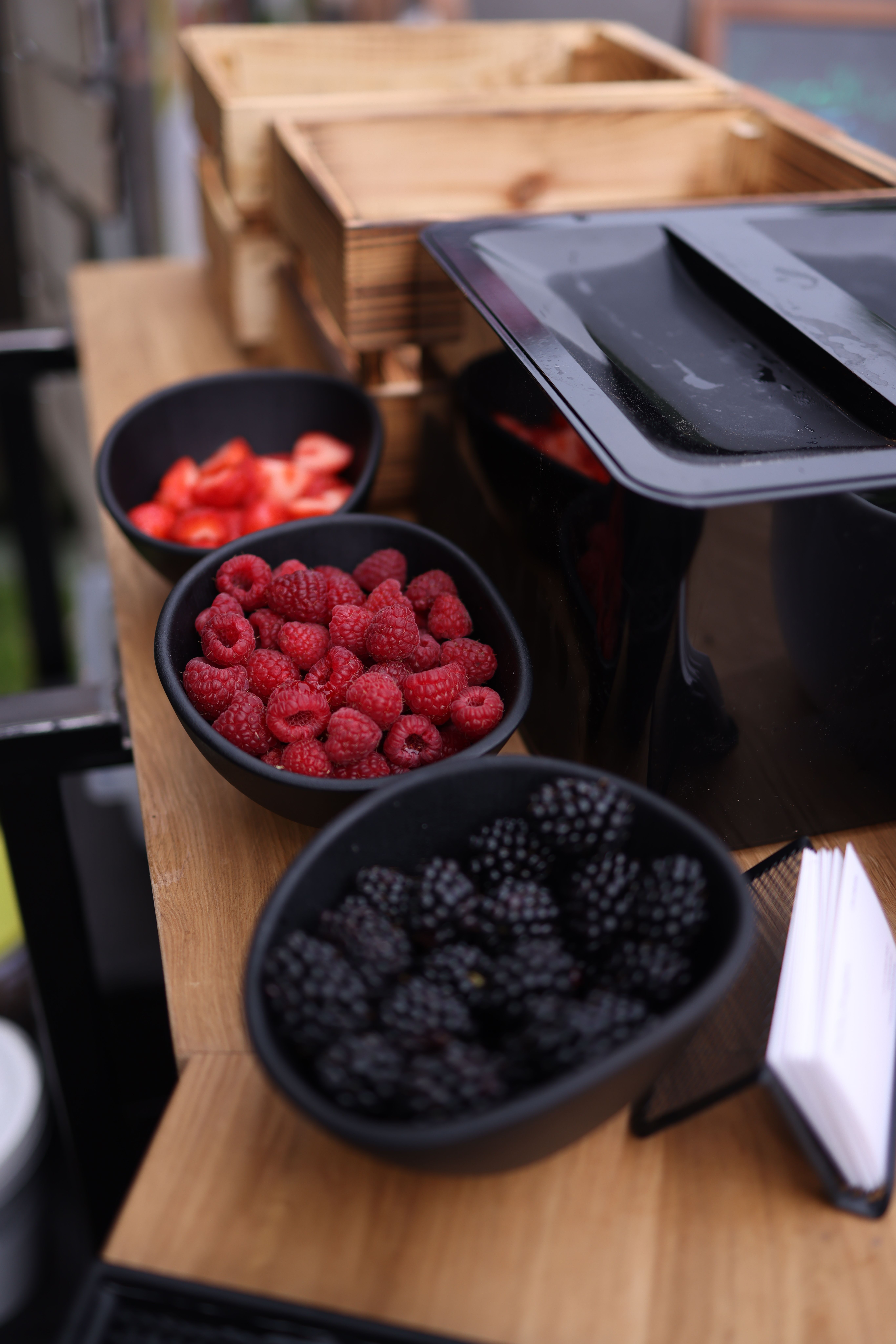 Fresh raspberries and blackberries displayed in black bowls on a stylish wooden table for a rustic food presentation.