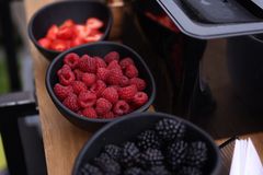 Fresh raspberries and blackberries displayed in black bowls on a stylish wooden table for a rustic food presentation.