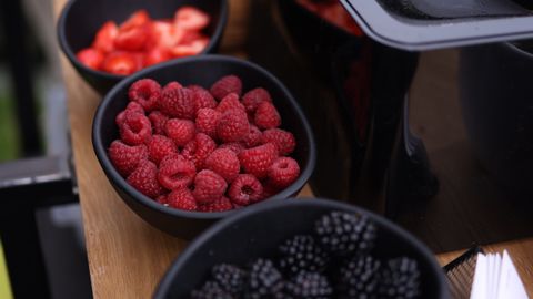 Fresh raspberries and blackberries displayed in black bowls on a stylish wooden table for a rustic food presentation.
