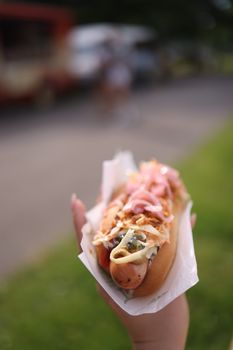 Close-up of a delicious hot dog topped with sauerkraut, mustard, and pickles outdoors.