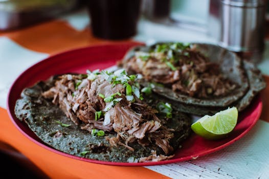 Close-up of delicious barbacoa tacos on a red plate with fresh lime in Ciudad de México.