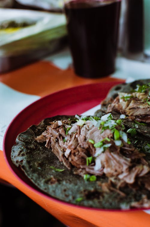 Two tacos on a red plate with green onions