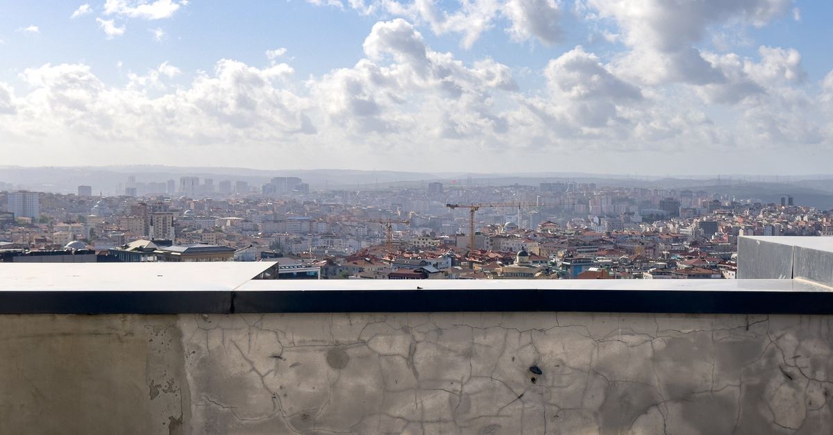 A panoramic view of a cityscape with rooftops, cranes, and dramatic clouds under a bright sky.