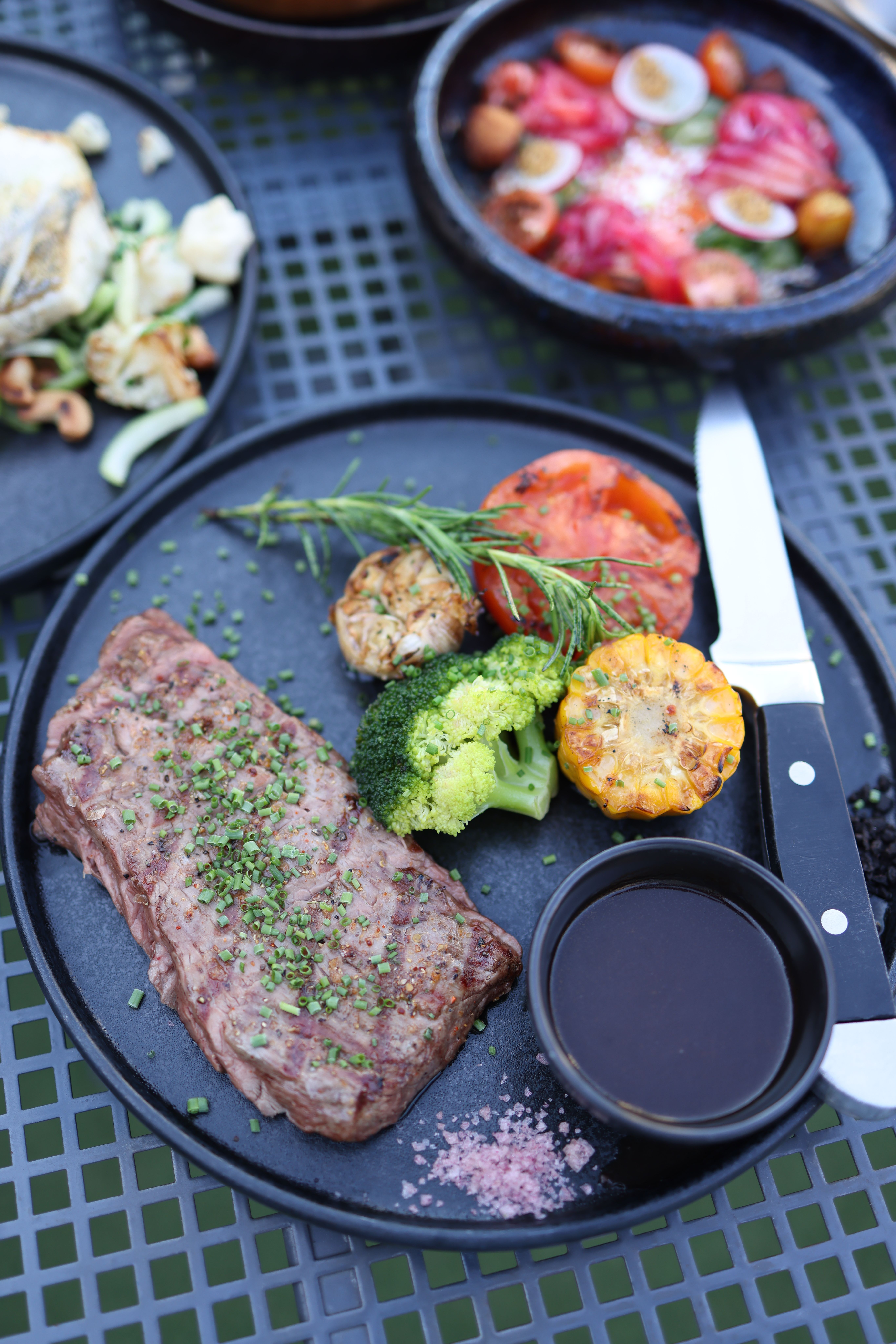 Delicious gourmet steak served with roasted vegetables and dipping sauce on a black plate.