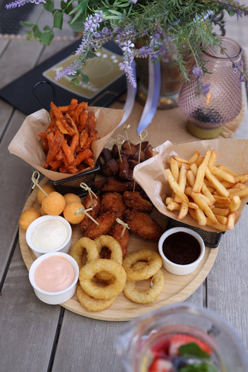 A wooden tray with food on it and a bowl of dipping sauce