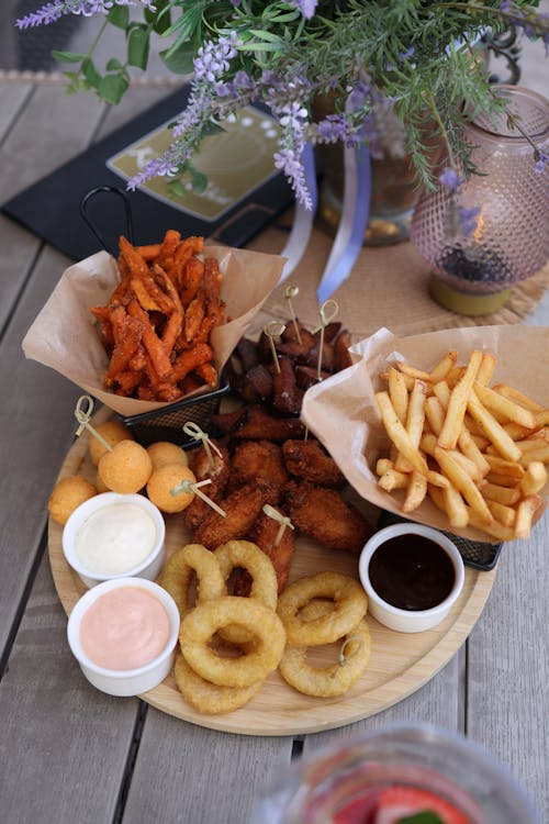 A wooden tray with fries, onion rings and dipping sauce