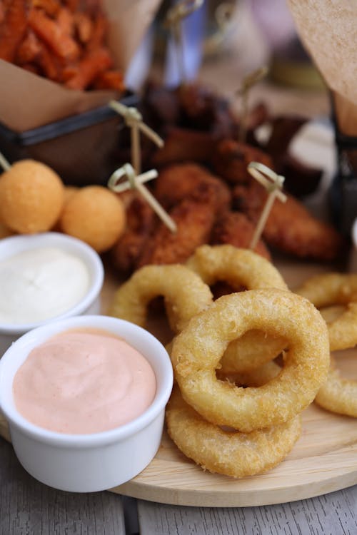 A wooden tray with fried onion rings, dip and other food