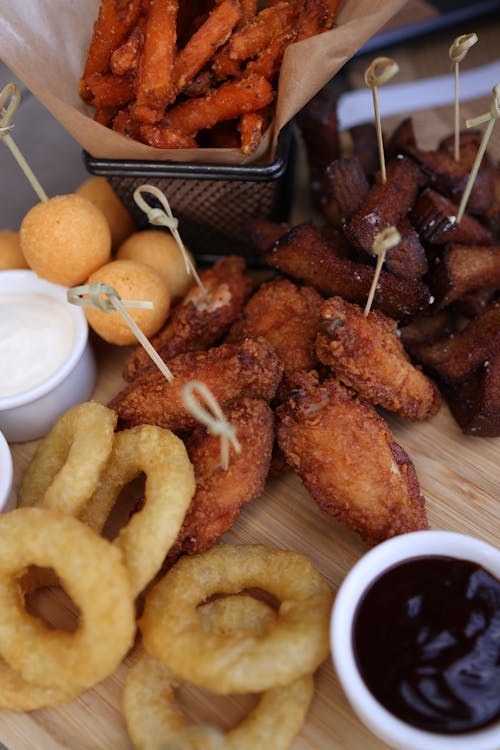 A wooden tray with fried chicken, onion rings and dipping sauce