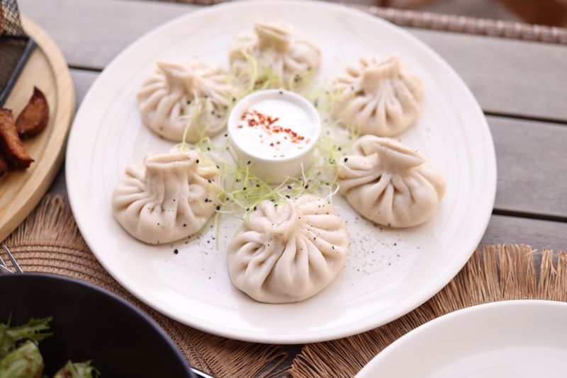 Plate of pleated dumplings with dipping sauce on a wooden table