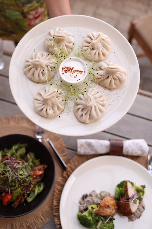 A person holding a plate of dumplings and salad