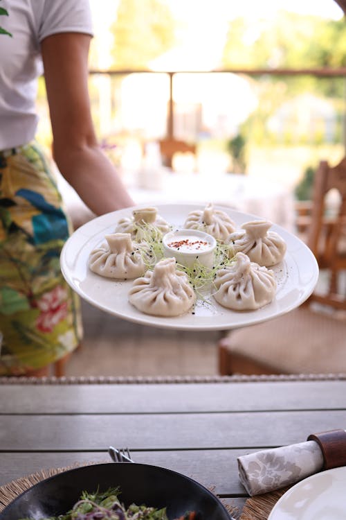 A woman holding a plate of dumplings in front of a table