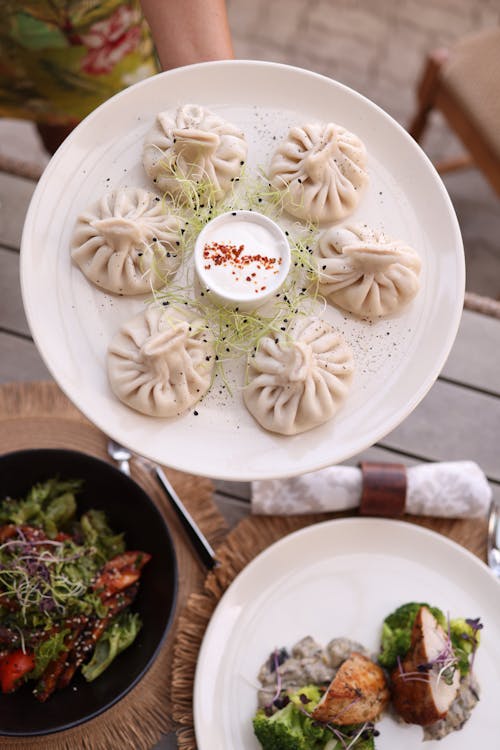 A person holding a plate of dumplings and salad