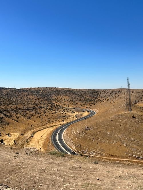 Free Winding road through dry Diyarbakır hills under a clear blue sky, highlighting nature's vastness. Stock Photo