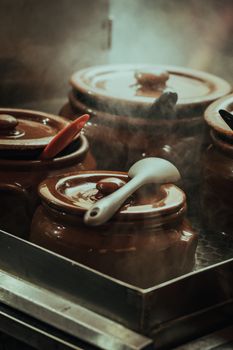 Close-up of steaming clay cooking pots with spoons in a rustic kitchen setting.