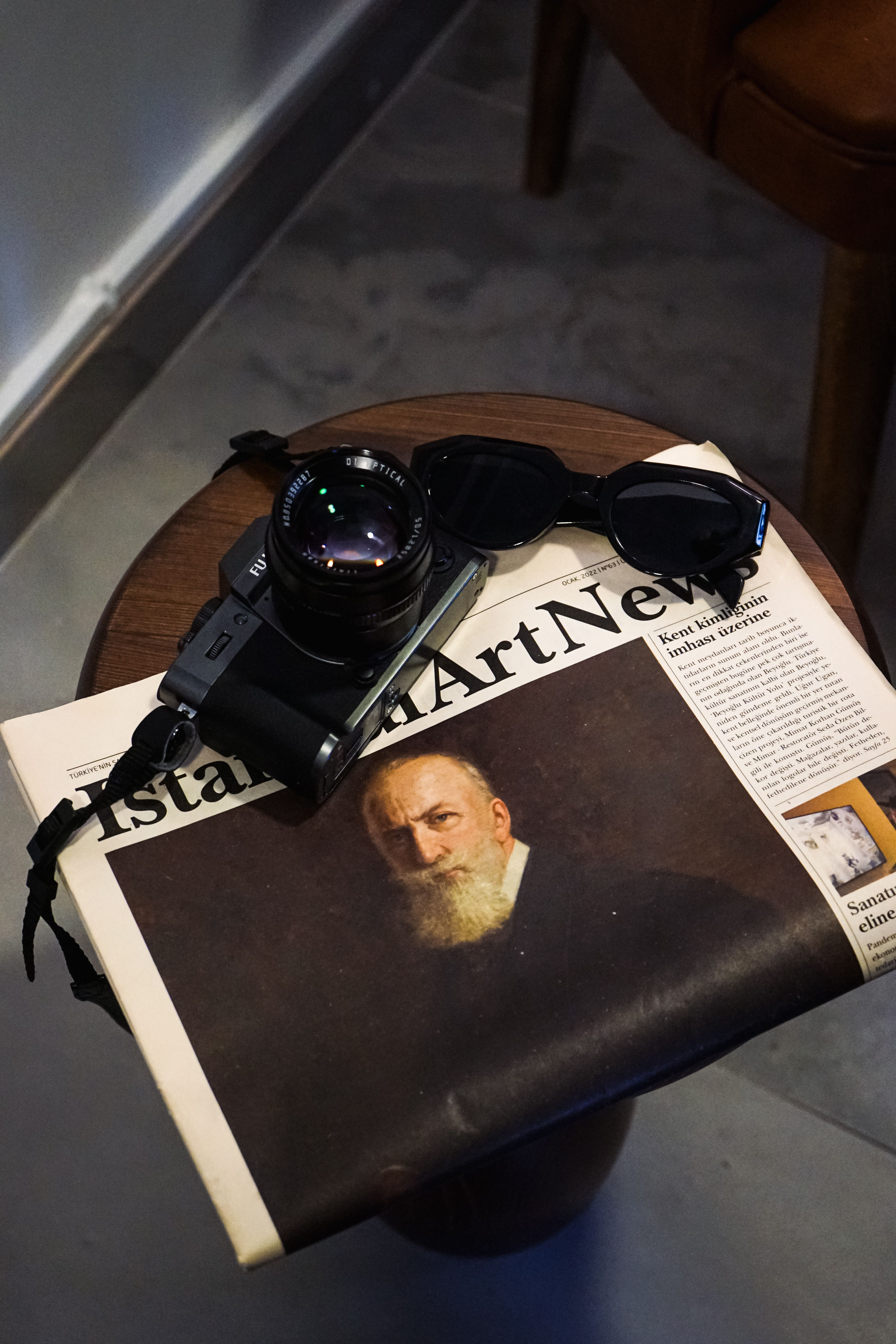 A stylish arrangement of a camera and sunglasses atop an art newspaper on a small table.