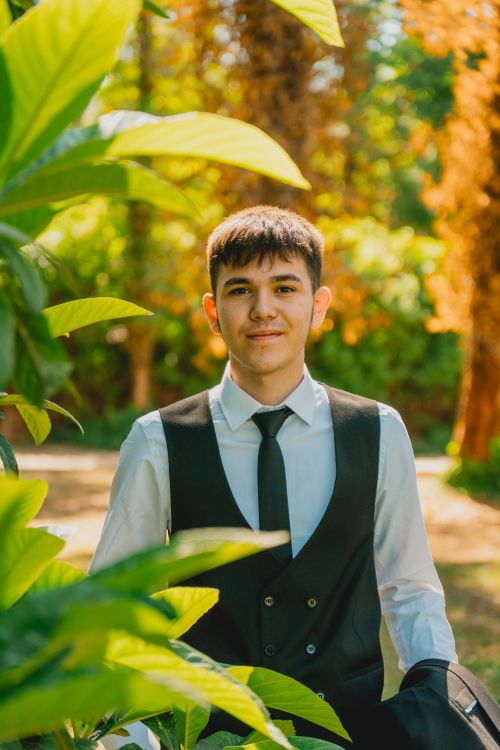 Free A young man in formal attire smiles surrounded by vibrant greenery outdoors. Stock Photo
