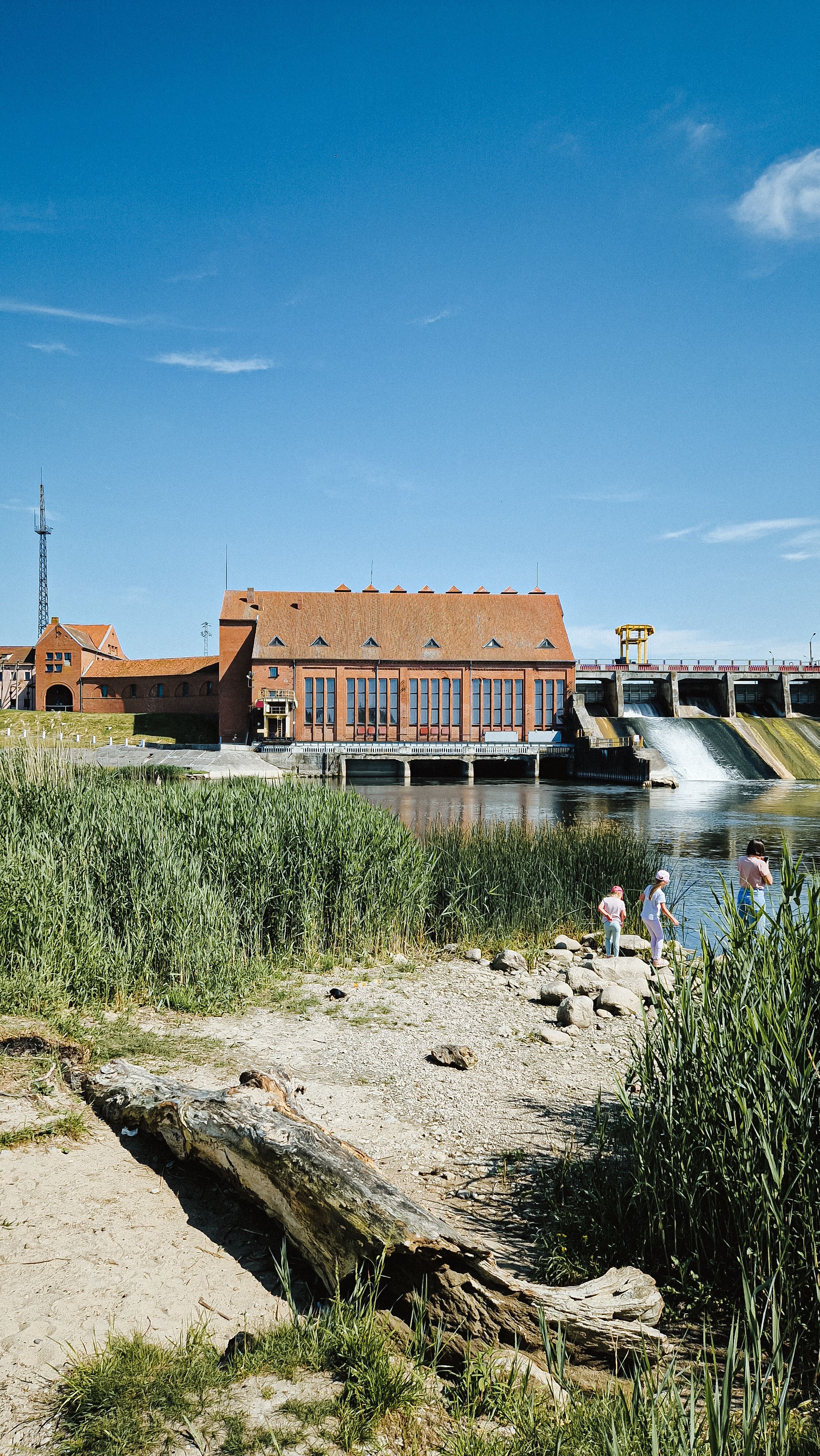 Hydroelectric power station with people enjoying nature nearby on a sunny day.